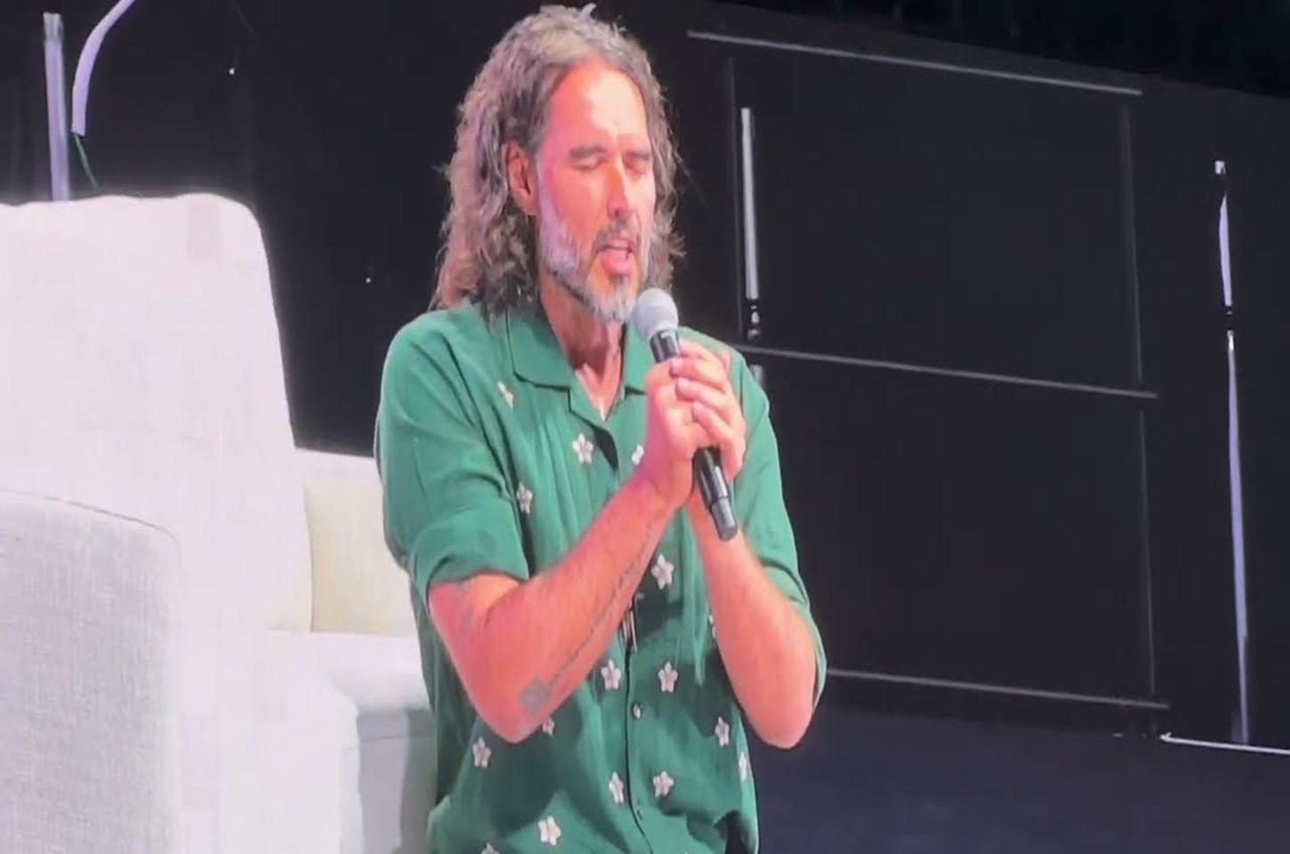 Russell Brand se ajoelha em oração no evento de Tucker Carlson, ora contra 'forças obscuras e demoníacas'